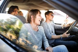 Cheerful young friends having fun in car. Young friends are enjoying in road trip. They are wearing casuals during summer vacation.